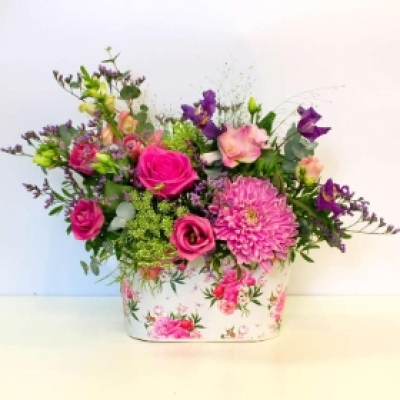 Ava - Beautifully presented in this floral container a collection of vibrant blooms.